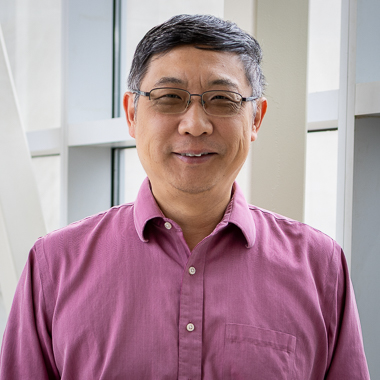Dr. Kefei Yu smiles at the camera. He's wearing a pink shirt and glasses and has a short hair cut. He looks very kind. 